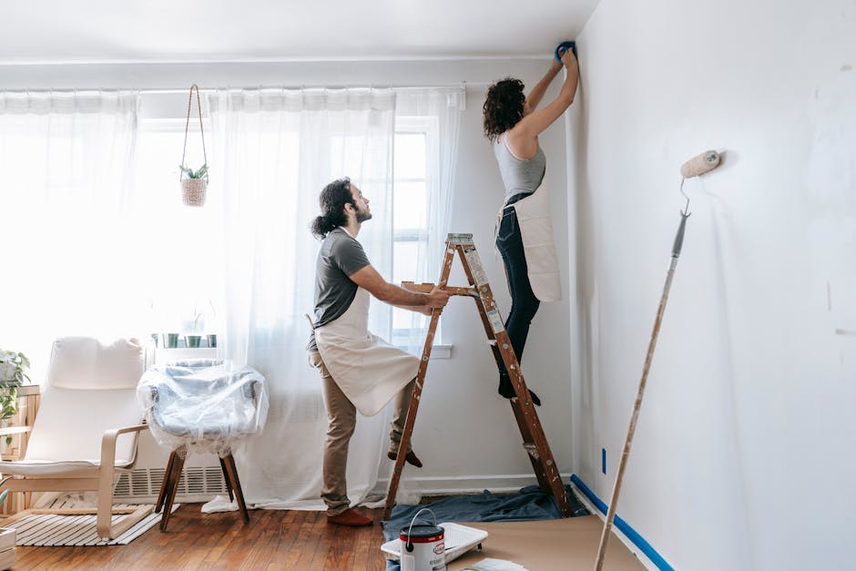 Couple renovating their home, with man supporting ladder and woman working on walls indoors.