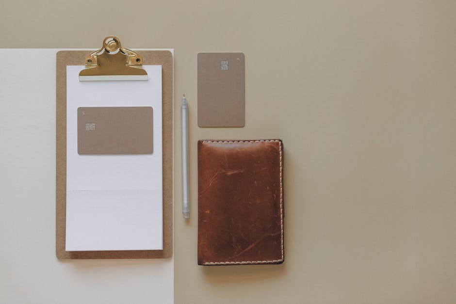 Flat lay of a minimalist office desk with clipboard, credit cards, pen, and leather wallet.