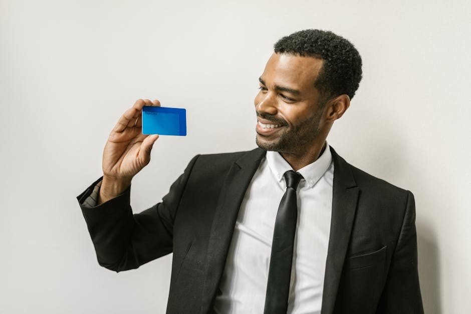 A confident man in a suit holds a credit card, smiling towards it.