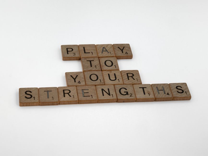 Motivational message 'Play to Your Strengths' made from wooden Scrabble tiles on a white background.