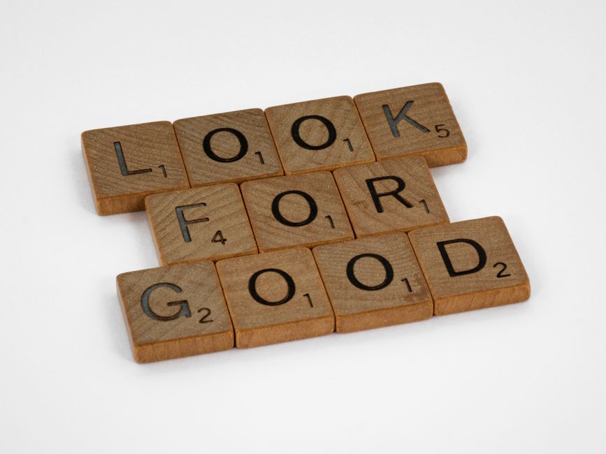 Close-up of wooden Scrabble tiles forming the phrase 'Look for Good' on a plain background.