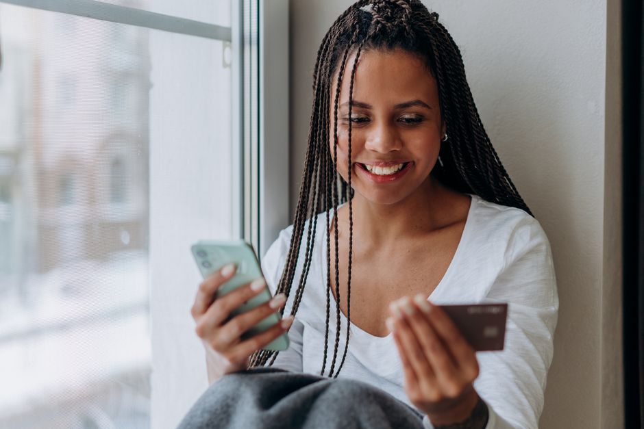 Smiling woman using smartphone and credit card for online shopping indoors with natural light.
