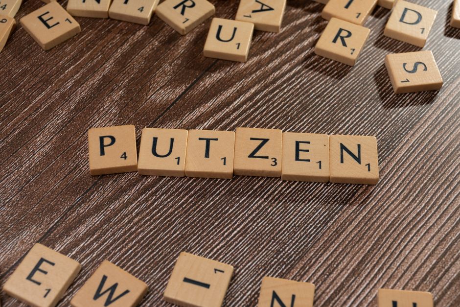 Wooden Scrabble tiles spelling the word 'PUTZEN' arranged on a brown wooden surface, top view.