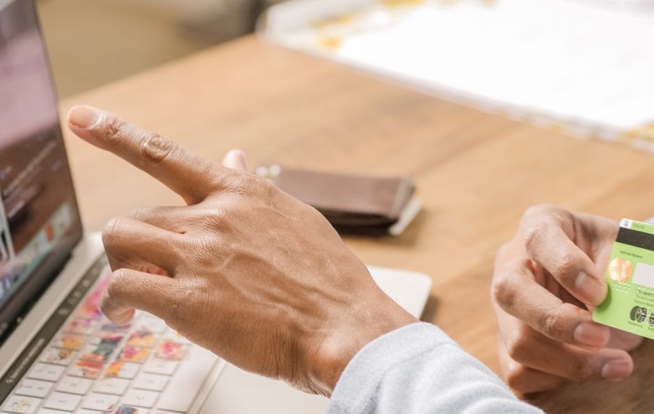 Person using a credit card and pointing at laptop for online shopping activity.