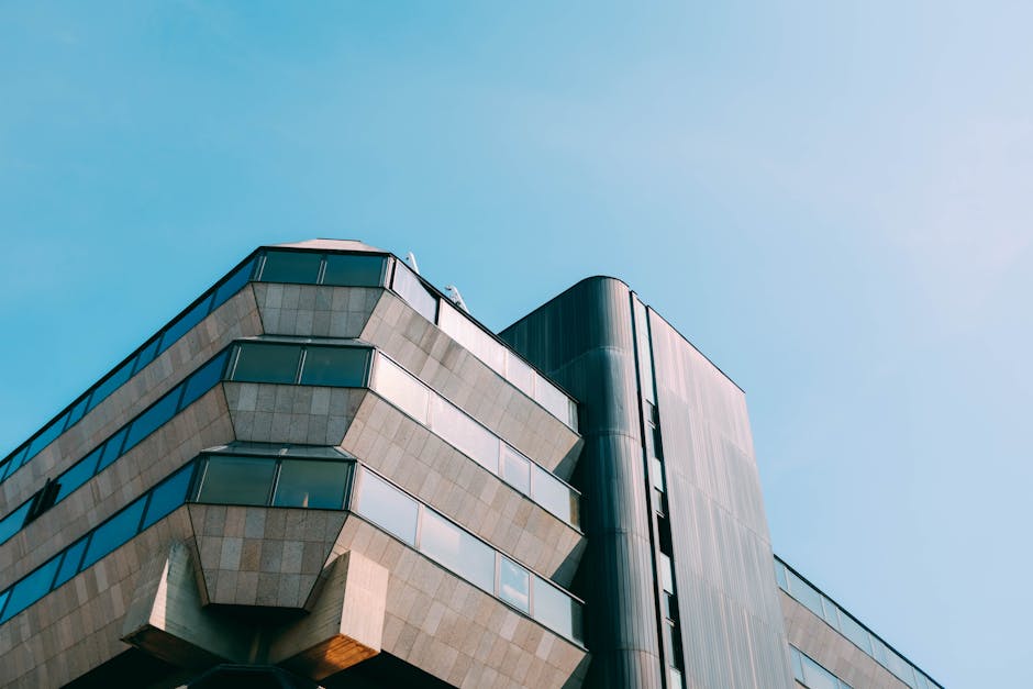 Low angle view of a modern geometric skyscraper against a clear blue sky, showcasing urban architecture.