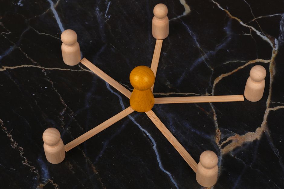Wooden figures arranged in network pattern on dark marble background, symbolizing communication.