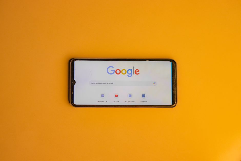 Smartphone displaying Google search page on a vibrant yellow background.