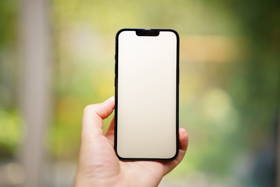 A hand holding a blank smartphone screen outdoors, ideal for mockups.