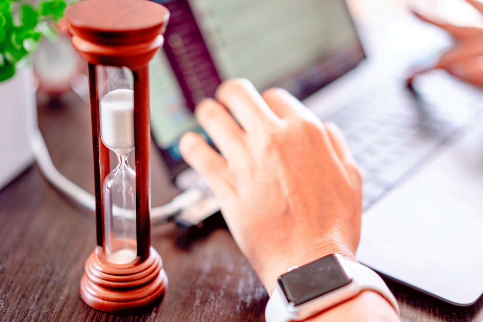 Close-up of a hand on a laptop with an hourglass, symbolizing time management and productivity.