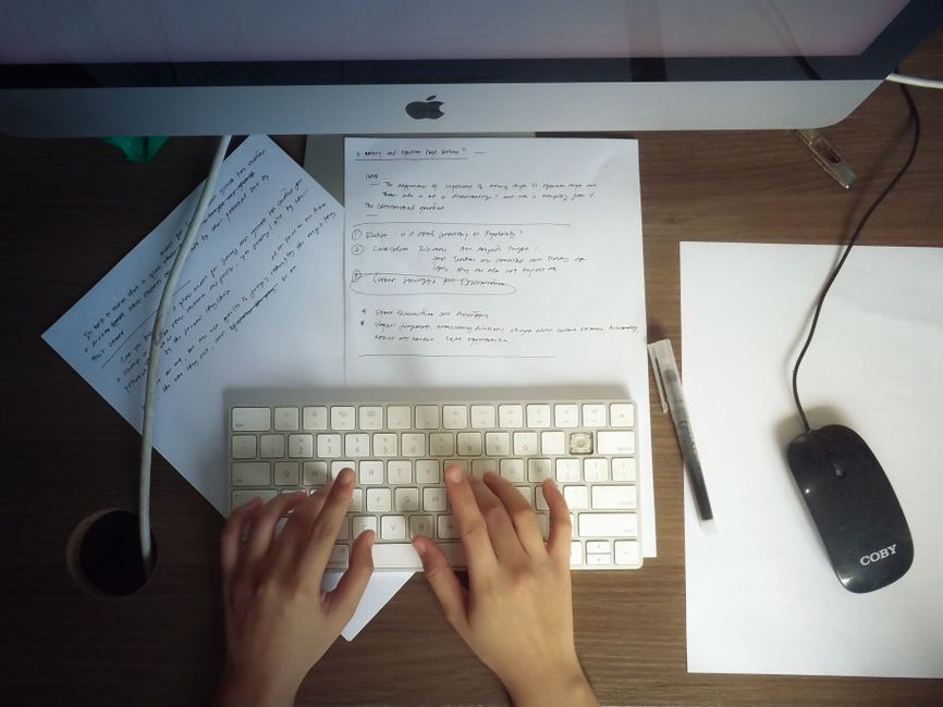 Hands typing on a keyboard at a wooden desk with papers and computer mouse visible.