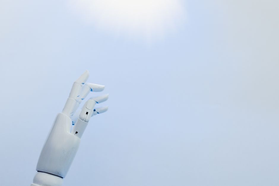 A robotic hand reaching towards a bright light on a white background symbolizing innovation.