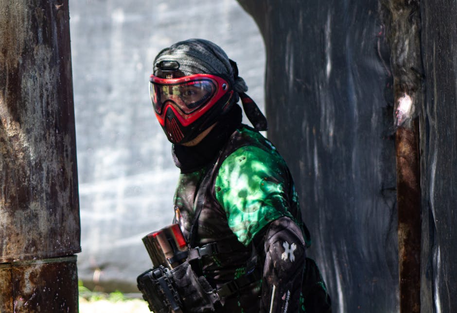 A paintball player in full gear and mask aiming during an outdoor match, showcasing intensity and focus.