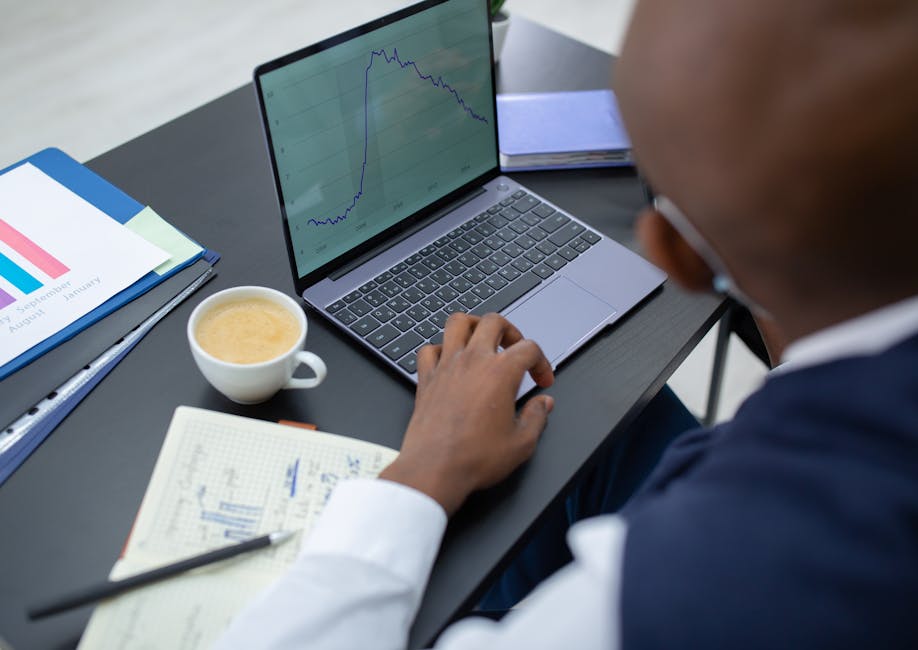 A professional adult reviewing financial charts on a laptop in a modern office.