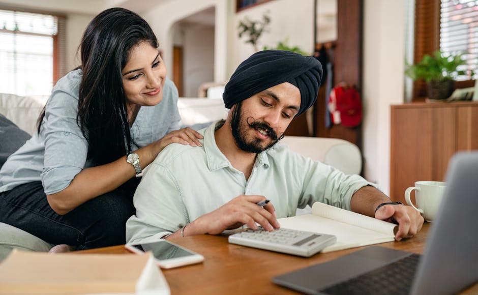 A cheerful South Asian couple reviewing finances with a calculator and notebook at home.