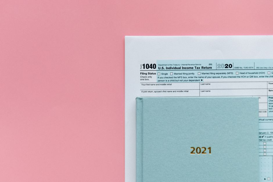 U.S. 1040 tax form with 2021 planner on a pastel pink background, symbolizing tax season.